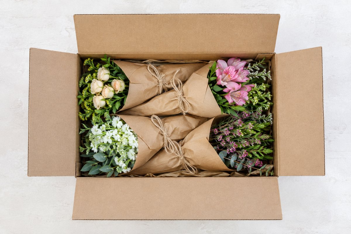 Platte kartonnen doos van boven gezien met vier in bruin papier gewikkelde bosjes bloemen
